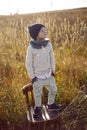 boy in warm clothes stand on chair along a path on a field with dried grass