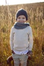 boy in warm clothes stand on chair along a path on a field with dried grass