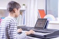 Boy watching video lesson at digital tablet computer and playing piano at home. Online learning remote education Royalty Free Stock Photo