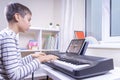 Boy watching video lesson at digital tablet computer and playing piano at home. Online learning remote education Royalty Free Stock Photo