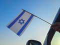 Boy waving Israel flag against the blue sky from the car window close-up shot. Man hand holding Israeli flag