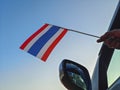 Boy waving Thailand flag against the blue sky from the car window close-up shot. Man hand holding Thai flag