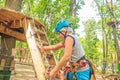 boy wearing blue helmet and climbing equipment climbs the stairs to the round wooden platform in the rope forest Royalty Free Stock Photo