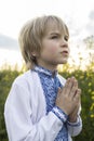 boy wearing a national Ukrainian embroidered shirt, folding his hands in prayer, turns to God Royalty Free Stock Photo