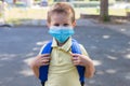 Boy wearing a protective mask with a backpack behind his back in the schoolyard on the first school day after isolation or Royalty Free Stock Photo