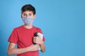 Boy wearing protective mask with books on light blue background, space for text. Child safety Royalty Free Stock Photo