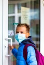 The boy wearing protective mask is trying to open the school door. Behind the backpack Schoolboy look aside Royalty Free Stock Photo