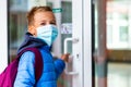 The boy wearing protective mask is trying to open the school door. Behind the backpack Schoolboy look at camera Royalty Free Stock Photo