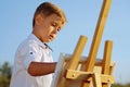Little boy wearing white shirt drawing on canvas outside