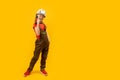 Boy wears helmet and working overalls holds drill in his hands. Child imitates builder, yellow background. Copy space, mock up