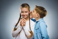 Boy whispering in ear of teen girl on gray background. Communication concept Royalty Free Stock Photo