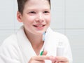 Boy, in a white coat, in the bathroom, holds a toothbrush and toothpaste in his hands, laughs