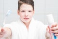 A boy in a white coat holds a toothbrush and a paste in front of him, close-up