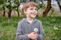 A boy with a white dandelion. Against the background of a blooming garden and green grass Royalty Free Stock Photo