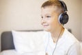 A boy in white T-shirt on the bed at home playing with pc tablet or reading online and listening to music with headphones Royalty Free Stock Photo