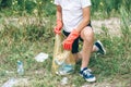 Boy in white t shirt in gloves collects garbage and plastic bottles into blue package on the beach.