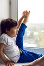 Boy in a white tank top and blue pants sits on a window Royalty Free Stock Photo