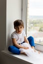 Boy in a white tank top and blue pants sits on a window Royalty Free Stock Photo