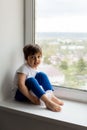 Boy in a white tank top and blue pants sits on a window Royalty Free Stock Photo
