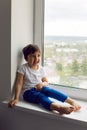 Boy in a white tank top and blue pants sits on a window Royalty Free Stock Photo