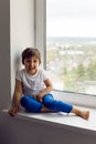 Boy in a white tank top and blue pants sits on a window Royalty Free Stock Photo