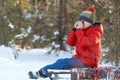 Boy in winter clothes sitting on a sled and covering his face with his hands and drinks tea