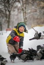 Boy in winter warm clothes feeds pigeons in city park. Pigeons in snow. Rescue birds in winter from hunger. Care for wild animals