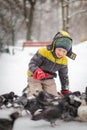 Boy in winter warm clothes feeds pigeons in city park. Pigeons in snow. Rescue birds in winter from hunger. Care for wild animals