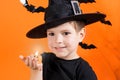 A boy in a witch costume in a black hat holds a small flashlight glowing pumpkin lamp Jack. on an orange background Royalty Free Stock Photo
