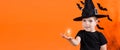 A boy in a witch costume in a black hat holds a small flashlight glowing pumpkin lamp Jack. on an orange background Royalty Free Stock Photo