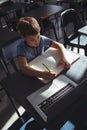 Boy writing in book by laptop at school