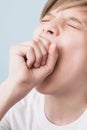 Boy yawns wide with his eyes closed, covering his mouth with his fist