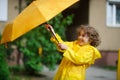 The boy 8-9 years in a bright yellow raincoat tries to hold an umbrella from wind flaws. Royalty Free Stock Photo