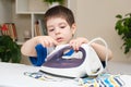 A boy of 4 years learns to hold an iron, iron clothes on an ironing board. Helper, help children to care for the house.