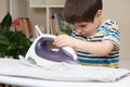 A boy of 4 years learns to hold an iron, iron clothes on an ironing board. Helper, help children to care for the house.