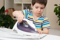 A boy of 4 years learns to hold an iron, iron clothes on an ironing board. Helper, help children to care for the house.