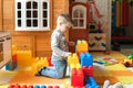 The boy is 4 years old, the blond plays on the playground indoors, builds a fortress from plastic blocks
