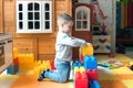 The boy is 4 years old, the blond plays on the playground indoors, builds a fortress from plastic blocks.