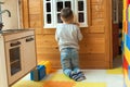 The boy is 4 years old, the blond plays on the playground indoors, peeps out the window of the toy wooden house