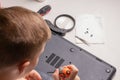 A boy of 10 years old is sorting a laptop for cleaning and maintenance. Selective focus. Screwdrivers, purge cylinder, magnifying