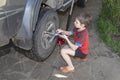 Boy 10 years old unscrews the nuts on the wheel of car. Wheel replacement in the yard Royalty Free Stock Photo