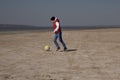 A boy of 10 years old in a white sweatshirt and orange vest plays football on a deserted beach in solitude