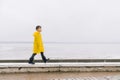 A boy in a yellow cloak raincoat is walking along the shore. G