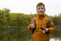 Boy in yellow jacket holding fishing rod outdoors at pond during cool autumn day