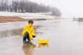 A boy in a yellow raincoat plays and launches in a puddle a large paper boat toy. Royalty Free Stock Photo