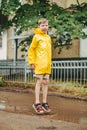 A boy in a yellow raincoat walks outside in the rain. A child jumps on the narrows. jump through muddy puddles.