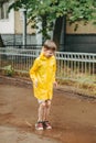 A boy in a yellow raincoat walks outside in the rain. A child jumps on the narrows. jump through muddy puddles.