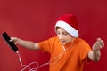 A boy in a yellow T-shirt and a red Santa hat holds a phone in his hands and listens to music through headphones Royalty Free Stock Photo