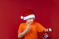 A boy in a yellow T-shirt and a Santa Claus hat holds a gift bag in his hand and shakes his fist at it Royalty Free Stock Photo