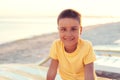 boy in yellow t-shirtsitting on bench near sea alone on beach at sunset. Happy family travel. Summer vacation with child